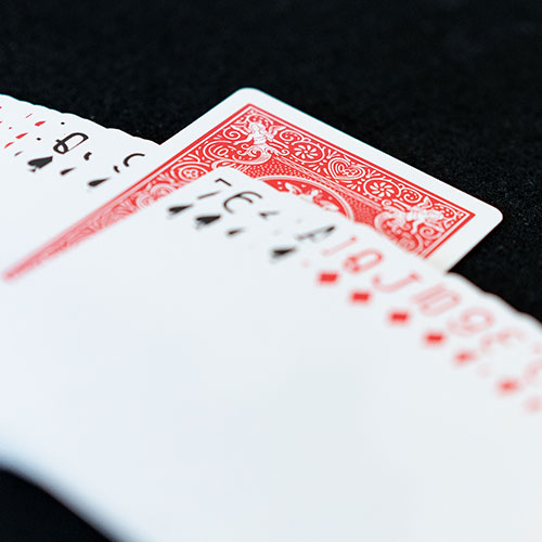 Deck of playing cards, face up, fanned out across dark background. One card in pack is facing down.