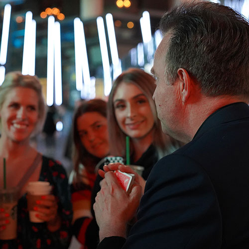 Interested onlookers eagerly awaiting Doug's reveal. He is holding a deck of cards in his hands.