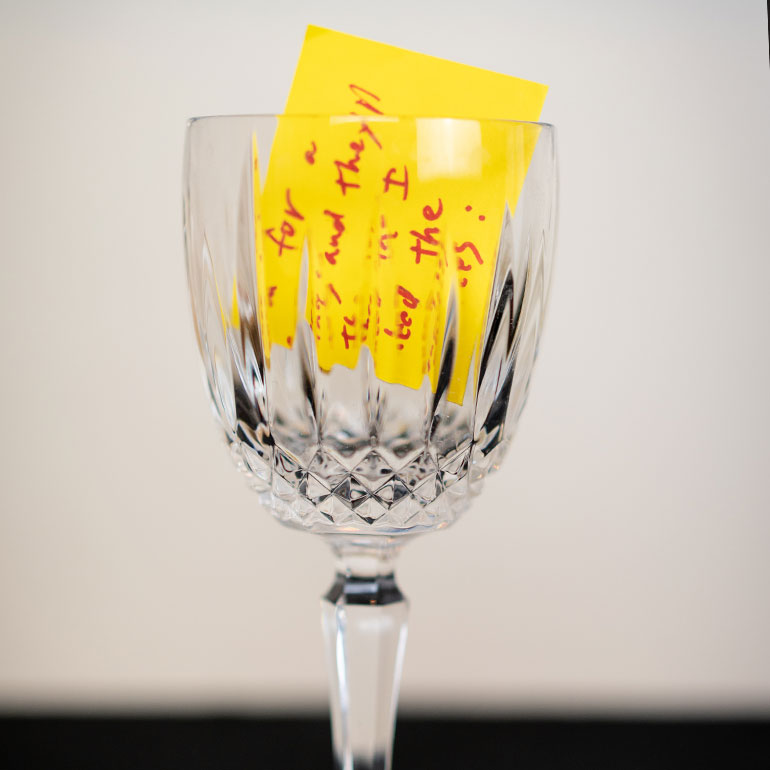 Semi see-through crystal drinking glass containing a piece of paper with writing on it.