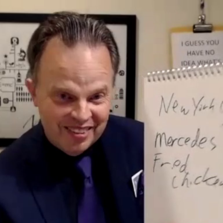 Doug next to a large, standing, note pad, with the words New York, Mercedes, and Fried Chicken, written on it.