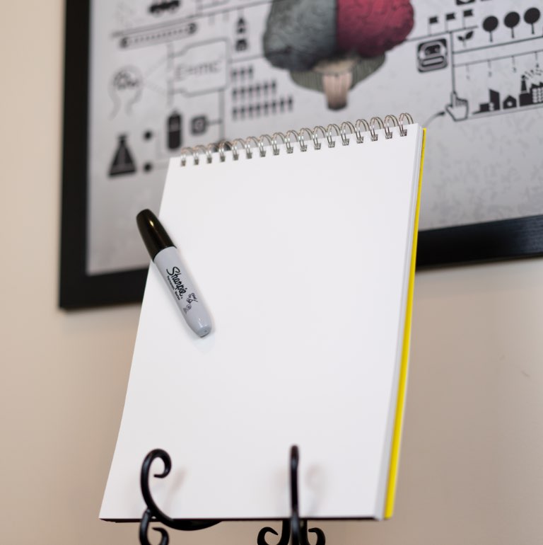 Blank note pad with a black felt marker clipped to it, resting on a stand.