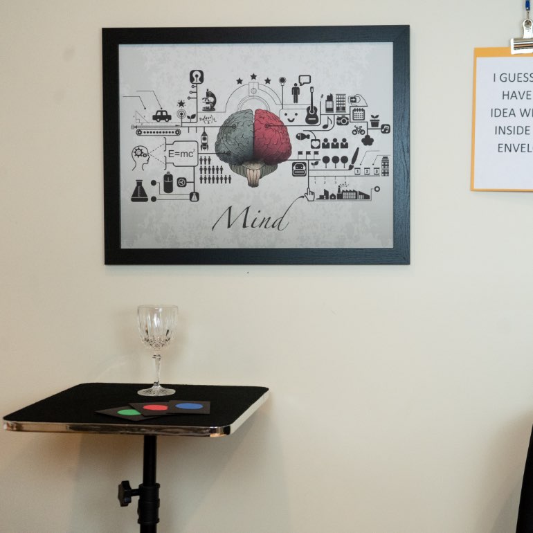 Crystal glass on a small table. 3 black envelopes with a colored dot on each sitting next to glass. Framed Mind picture on wall.